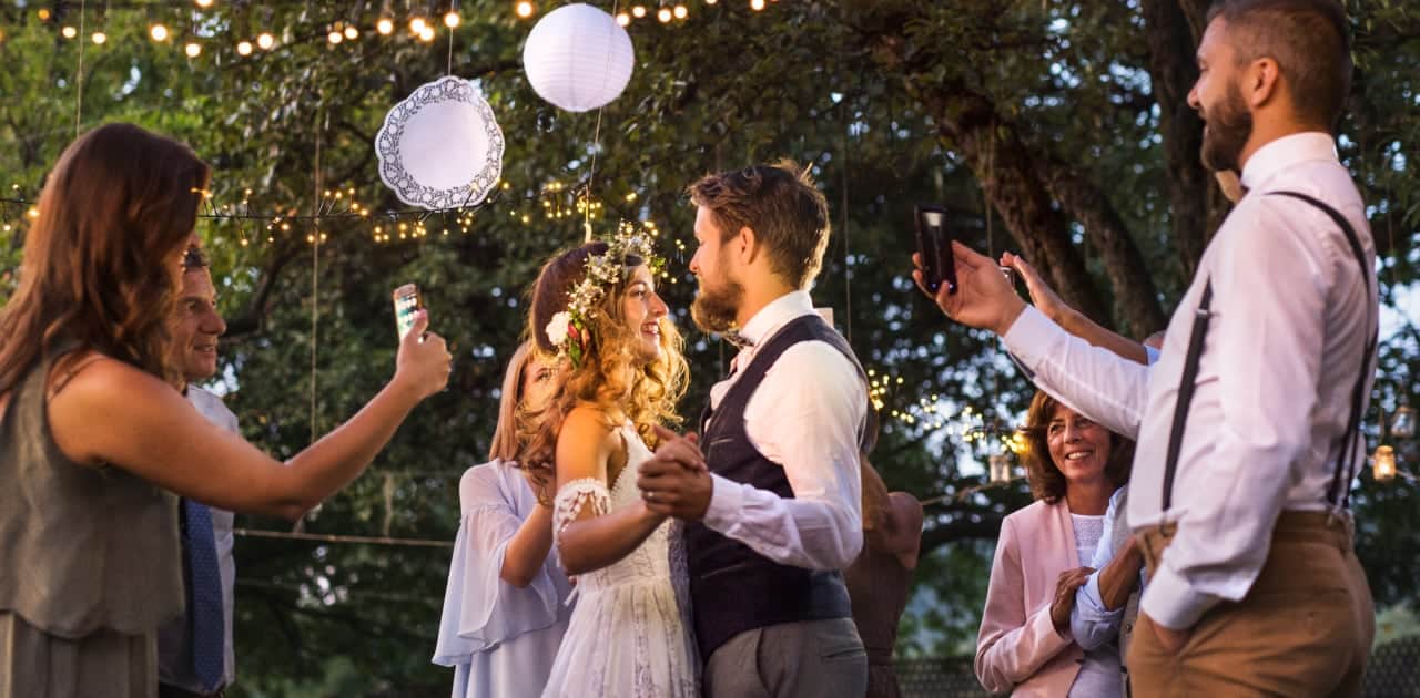 Bride and groom dancing outdoors with friends taking photos around them