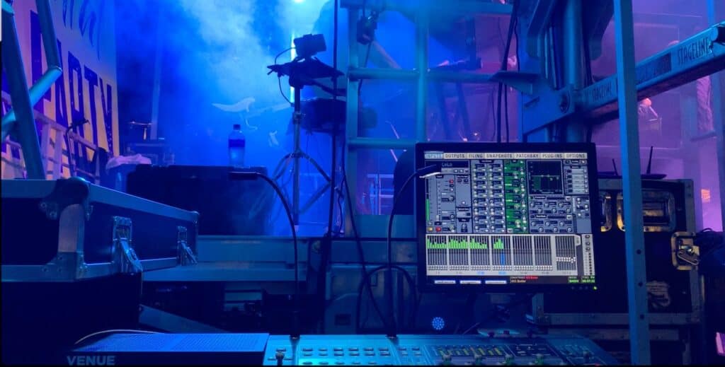 A light control panel and monitor backstage under blue and purple lights and fog effects.