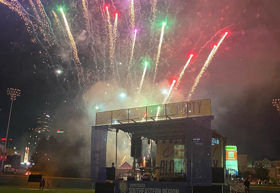 A photo of a stage with pipe and drape banners at night, complete with bright and colorful fireworks exploding overhead.