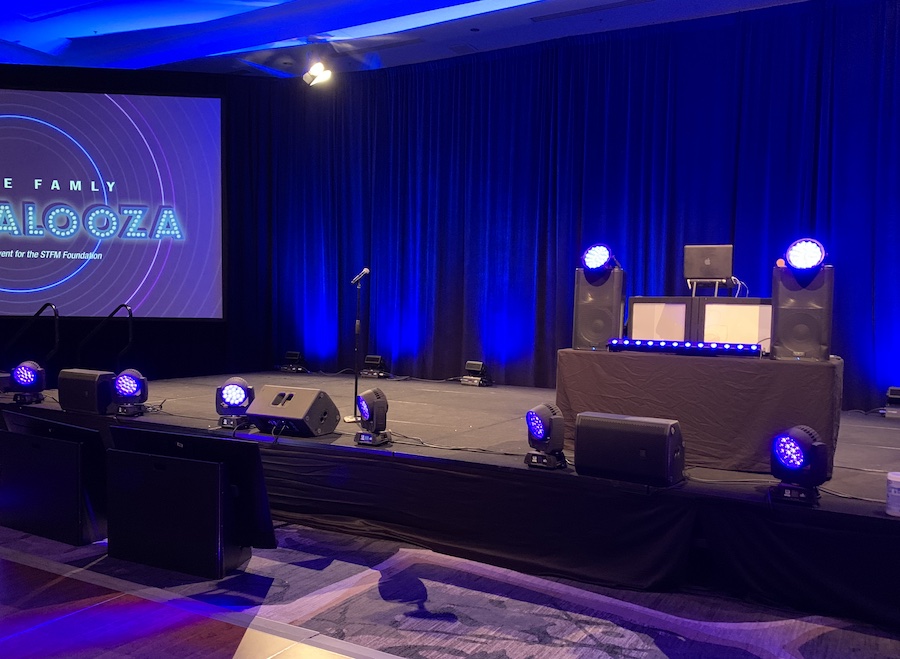 An event stage with a screen, blue drapes, lights, and audio equipment like speakers and microphones