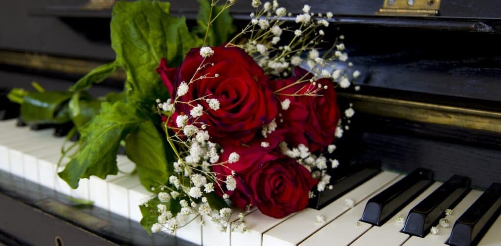 A red rose rests on a piano's keys